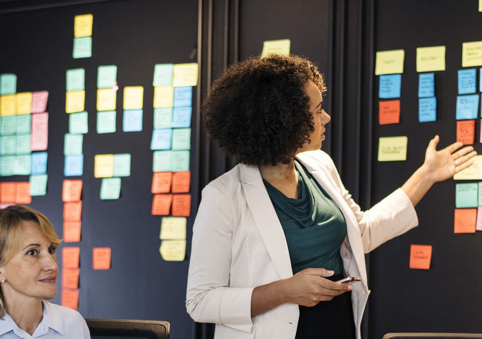 Uma equipe multidisciplinar de profissionais da saúde reunida em frente a um quadro Kanban, discutindo estratégias e melhorias nos processos hospitalares.