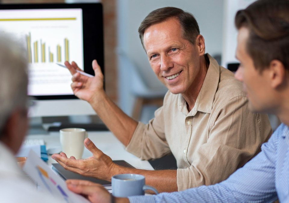 Reunião de equipe em um ambiente corporativo de saúde, com profissionais analisando dados e gráficos de programas de promoção e prevenção em saúde.