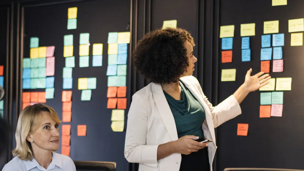 Uma equipe multidisciplinar de profissionais da saúde reunida em frente a um quadro Kanban, discutindo estratégias e melhorias nos processos hospitalares.